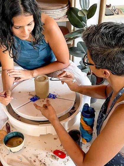 A close up of hands on guidance, as I help a student with the delicate process of shaping her piece on the wheel.