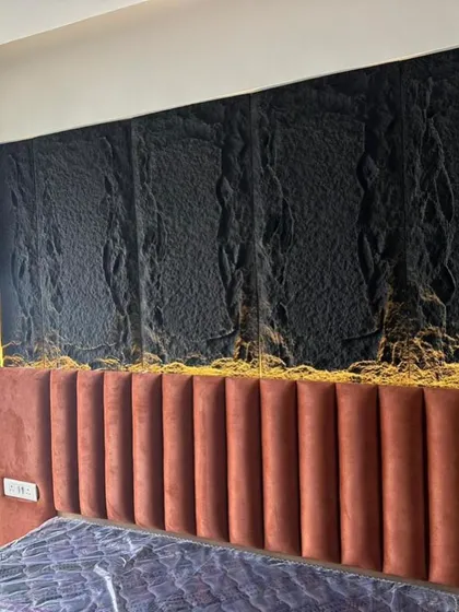 A close-up of the bedroom's feature wall, showing the detail of the textured black stone-like panels and the plush fabric of the headboard. This demonstrates our focus on material combination.