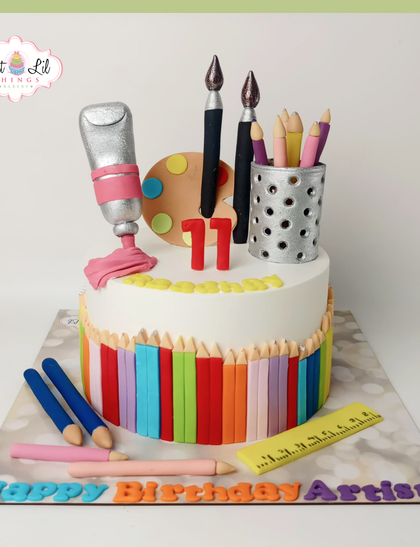 A clean and colorful artist cake, perfect for an 11th birthday. The base is wrapped in a rainbow of edible colored pencils, and the top is decorated with fondant art supplies.