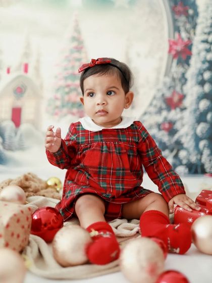 Her first Christmas is full of wonder. This baby girl looks so curious and sweet in her festive plaid dress, surrounded by holiday decorations.