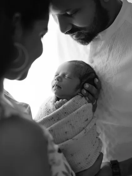 A precious moment captured in black and white. This artistic shot focuses on the parents' hands cradling their newborn, emphasizing the feeling of protection and love.