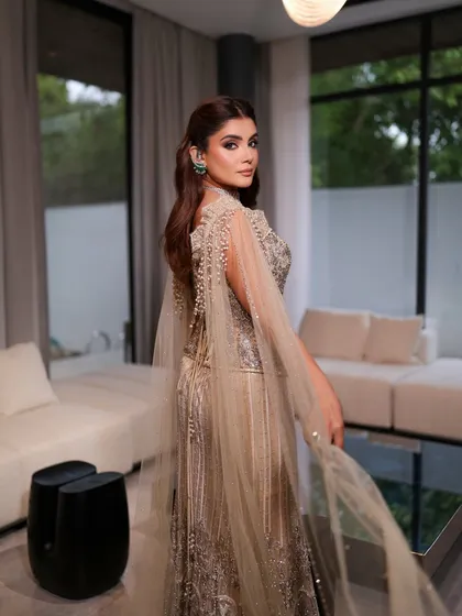 A beautiful shot from the back, showing the flow of the gown's cape. The makeup remains flawless, with a focus on glowing skin that catches the light as she moves.