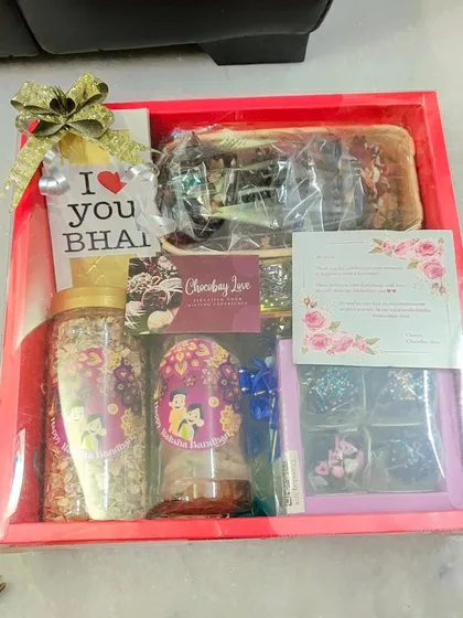 A large, open-faced Rakhi hamper box. This one includes a chocolate bar, jars of cookies and muesli, a box of truffles, and a cake loaf.