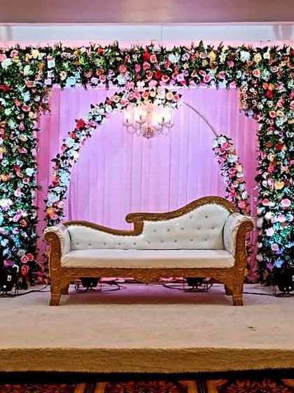 This reception stage at Jashan Banquet hall features three floral arches over a soft pink curtain backdrop. The design provides a wide, elegant space perfect for the couple and their families on stage.