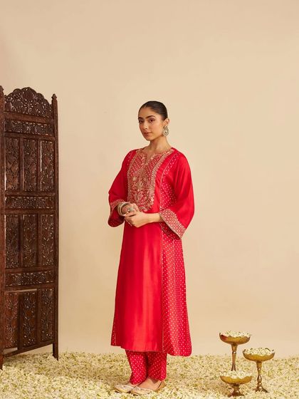 A stunning red kurta set with gold embroidery, styled against a traditional screen, embodying classic festive elegance.