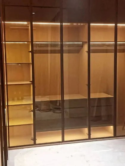 An open view of a walk-in wardrobe during installation. You can see the internal configuration with hanging rods, shelving, and a chest of drawers, all illuminated by profile lighting.