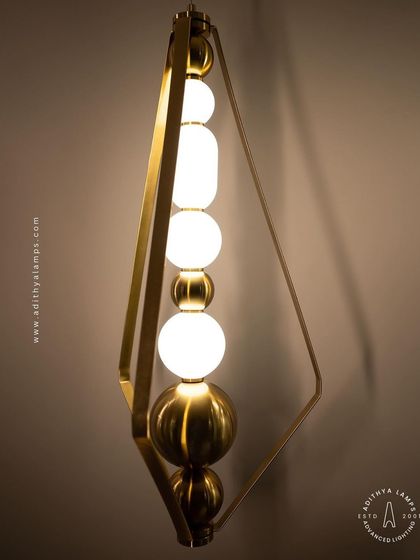 This elegant pendant is framed by a triangular gold structure, enclosing a string of white and gold beads. It's a sophisticated and modern piece that adds a touch of jewelry-like decoration to your space.