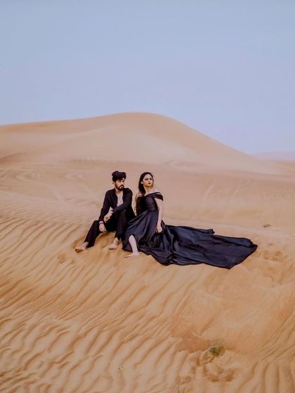 A serene moment captured in the vast Dubai desert. The couple sits together on a sand dune, creating a peaceful and intimate portrait against the immense, quiet landscape.
