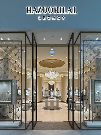 The entrance to the Hazoorilal Legacy store in Dubai Hills Mall is designed to be open and inviting. The full-glass facade offers a clear view into the serene and luxurious interior, where a grand chandelier and curved forms welcome visitors.