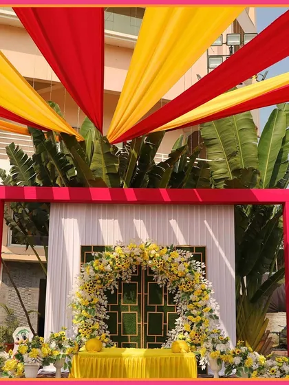 A vibrant 'Satrangi' themed Mehendi decor, with a floral arch in bright yellow and pink, and colorful drapes creating a festive canopy.