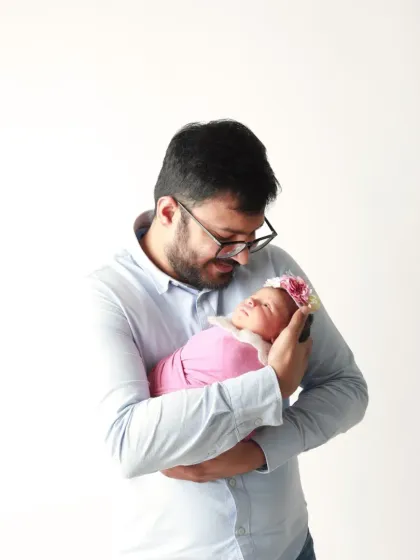 A proud new father cradles his swaddled baby girl. A simple, clean, and emotionally powerful studio portrait.