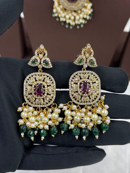 Close-up of the earrings from our peacock-motif necklace set. The design features ruby stones and green and white pearl droppings.