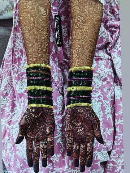 A beautiful contrast between the dark stain on the hands and the lighter, faded pattern on the arms, paired with traditional green bangles.