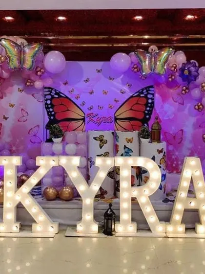 A full view of the "Kyra" butterfly-themed stage decoration, showing the large marquee letters and pink and purple balloon decor.