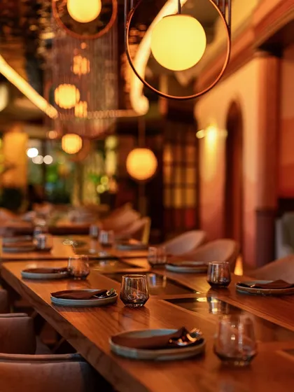 A long, communal table set for dinner. The warm, glowing lights and carefully set plates invite you to gather with friends for a memorable meal.