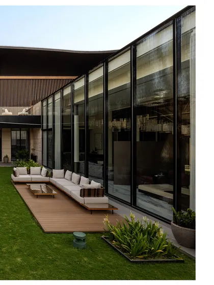 The L-shaped layout of Residence Ondra is built around a central lawn, blurring the lines between the interior and the exterior. A wall of glass provides uninterrupted views of the garden, while the wooden deck and comfortable outdoor seating extend the living space into nature, creating a perfect setting for relaxation.
