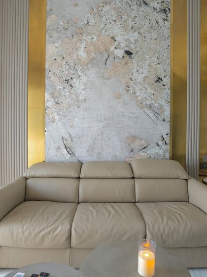 The den bedroom in the 'Urban Oasis' project, designed as a multi-functional space. A comfortable leather sofa is set against a wall with abstract art and metallic gold accents.