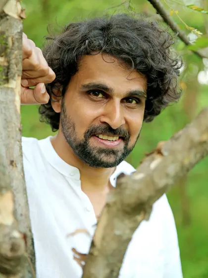 A pleasant, close-up portrait of a male model in a simple white shirt, framed by tree branches. This natural and authentic portrait style is effective for lifestyle brands.