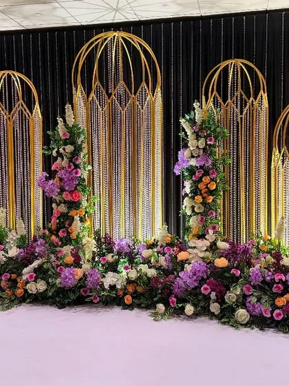 An elegant and sophisticated stage design featuring Art Deco inspired golden arches and a bed of rich purple flowers. This setup combines modern structural elements with classic floral beauty for a truly unique look.