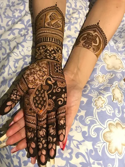 This design incorporates traditional Indian wedding symbols, including a peacock on the palm and a doli (palanquin) on the forearm.