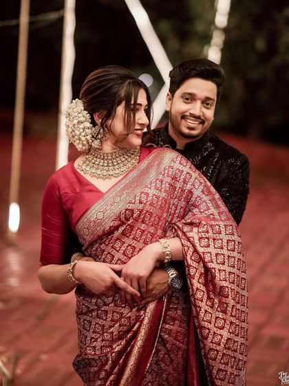 A beautiful reception photo. The groom looks dashing in a black sherwani, perfectly complementing his bride's stunning red saree.