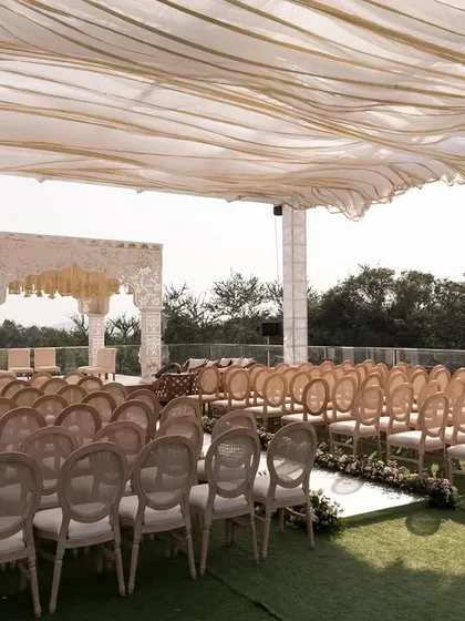 A wide view of a rooftop wedding ceremony in Alibaug, featuring a modern white mandap and a flowing fabric canopy that adds softness and shade.