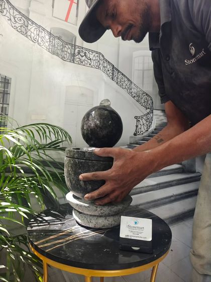 An artisan assembles a small granite fountain, showing how the sphere sits atop the bowl. This piece is hand-carved from a single block of granite.