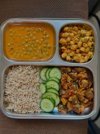 This colorful plate includes brown rice, green peas curry, sautéed brinjal, and a chickpea side, with fresh cucumber for a refreshing crunch.