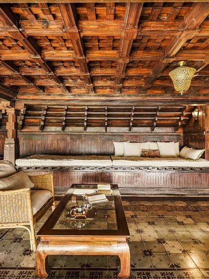 A cozy seating area within a heritage building, featuring intricate wooden ceilings and traditional furniture. Sunlight streams in, creating a warm and inviting space for relaxation.