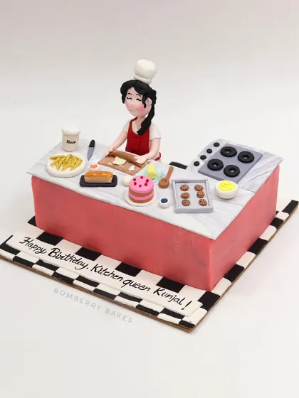 A cake for a "Kitchen Queen," featuring a detailed kitchen scene with a chef figurine, stove, and tiny edible baked goods.