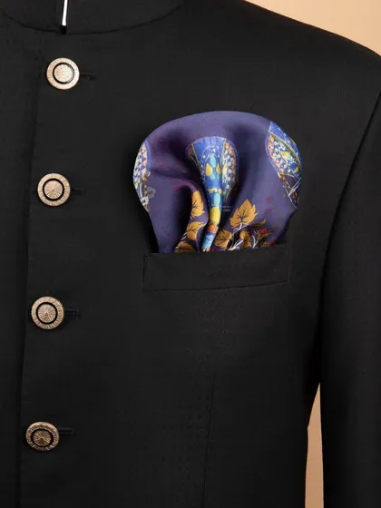 A detailed lifestyle shot of a navy blue patterned pocket square neatly folded in the pocket of a black bandhgala jacket.