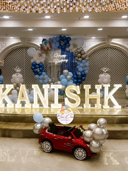 A grand space-themed first birthday on a stage, with marquee letters, a circular balloon arch, and a toy car.