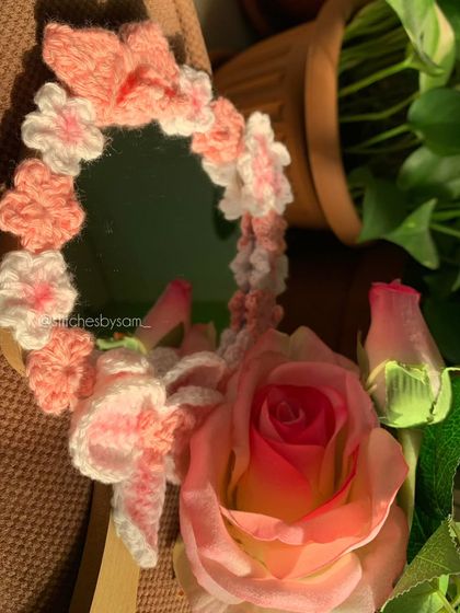 A close up shot of the crochet pink flower mirror, showing the detail of the different flower styles and the bow. It's a perfect girly accessory for a makeup table.