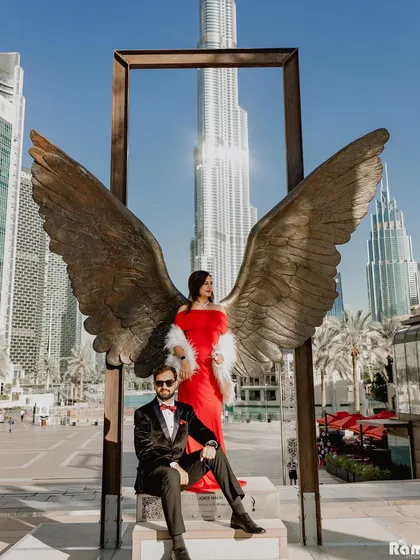A powerful and stylish portrait of the couple posing with the iconic angel wings sculpture in Dubai. The groom's seated pose complements the bride's standing elegance, creating a balanced and glamorous shot.