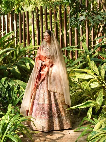 A wide shot showing the bride in a beautiful garden. Her pastel lehenga and glowing makeup make her look like she's stepped out of a fairytale.