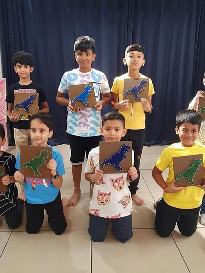 A group of boys proudly show off the dinosaur string art they made at a birthday party. Art is for everyone.
