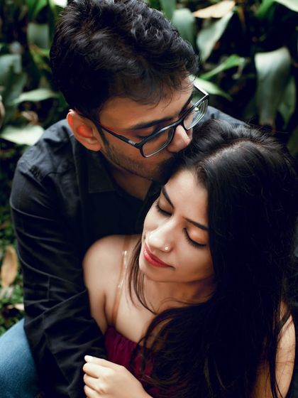 An intimate portrait where he gently kisses her forehead. The dark, moody green background makes the moment feel private and deeply personal.