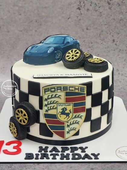 A Porsche-themed cake with a checkered flag pattern. This design includes the Porsche crest, a car topper, and edible tires.