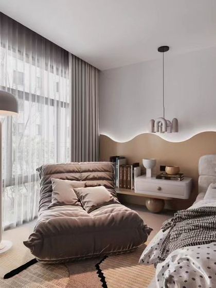 A cozy and modern bedroom corner featuring a comfortable lounge chair and a unique wavy headboard with backlighting. This design shows how we create relaxing nooks within a larger space.