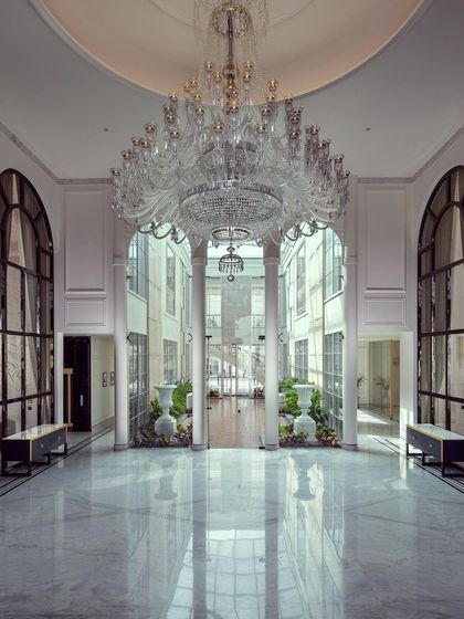 The grand foyer of The Grand Alabaster is a breathtaking introduction to the home's palatial scale. A massive crystal chandelier hangs from the high ceiling, its light reflecting off the polished marble floor and creating a dazzling effect.