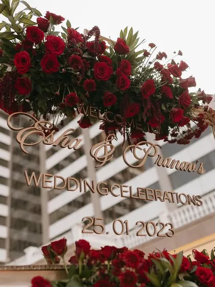 A welcome sign for a wedding celebration, featuring an ornate gold-framed mirror with custom lettering and a lush arrangement of red roses.