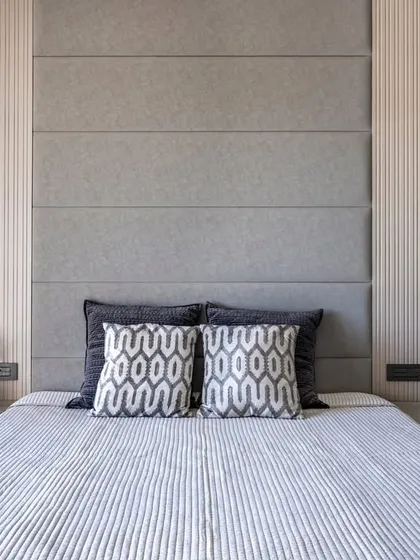 A focus on the bed and headboard, this image shows the layering of textures, from the vertically striped wallpaper to the paneled fabric headboard and patterned cushions.