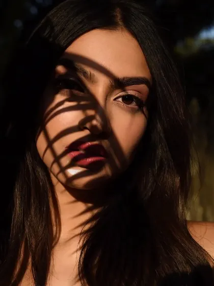 The shadow of a leaf creates a beautiful, organic pattern on the face, adding an artistic touch to the makeup.
