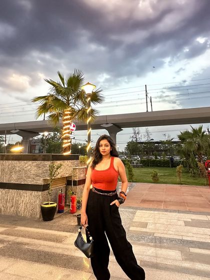 The full outfit against a dramatic cloudy sky. The orange top really pops against the moody background.
