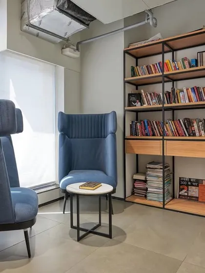 A quiet reading corner with high-backed blue armchairs that provide visual and acoustic privacy. A small bookshelf makes it a perfect spot to unwind.