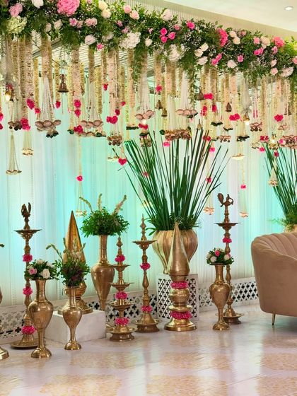 A beautiful stage-side arrangement featuring a variety of traditional brass lamps and pots, decorated with pink flowers, enhancing the cultural feel of the event.