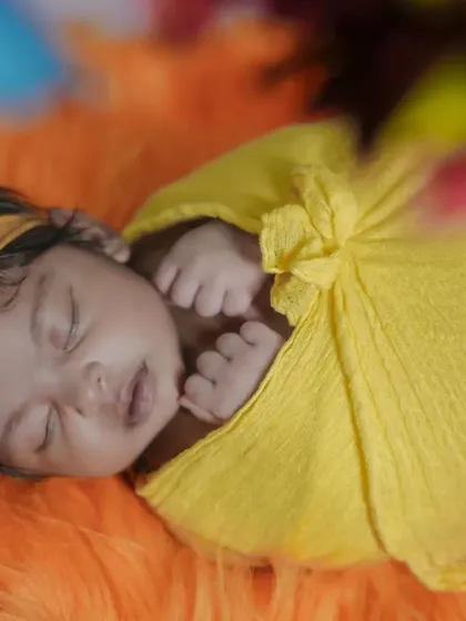 A close-up of a newborn wrapped in yellow, showing the delicate texture of the wrap and the baby's tiny, curled fingers.