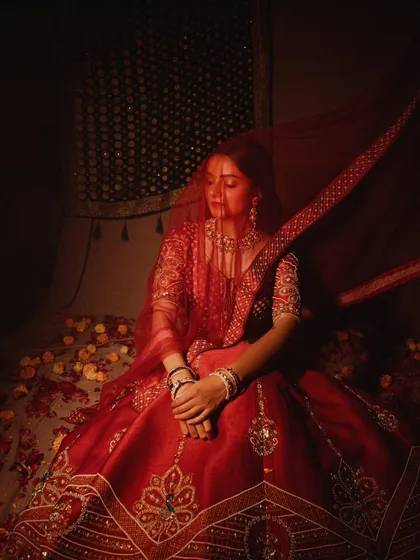 A quiet, contemplative moment from a bridal story. The model is surrounded by soft fabrics and flower petals, creating a dreamy and romantic atmosphere.