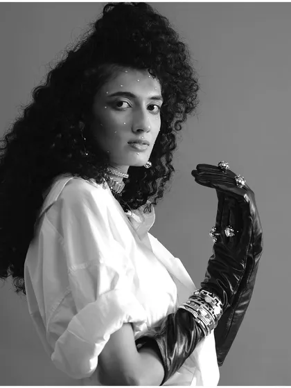 A black and white version of an experimental portrait, focusing on texture and form. The absence of color highlights the sparkle on the model's face, the curls of her hair, and the sheen of the leather glove.