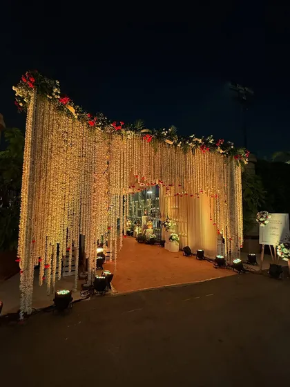 A grand entrance at night, with a massive curtain of hanging flowers illuminated by spotlights, creating a dramatic and beautiful effect.
